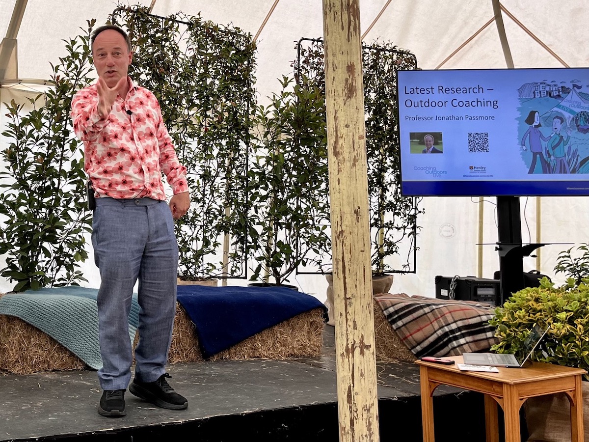 man speaking on stage with plants and screen